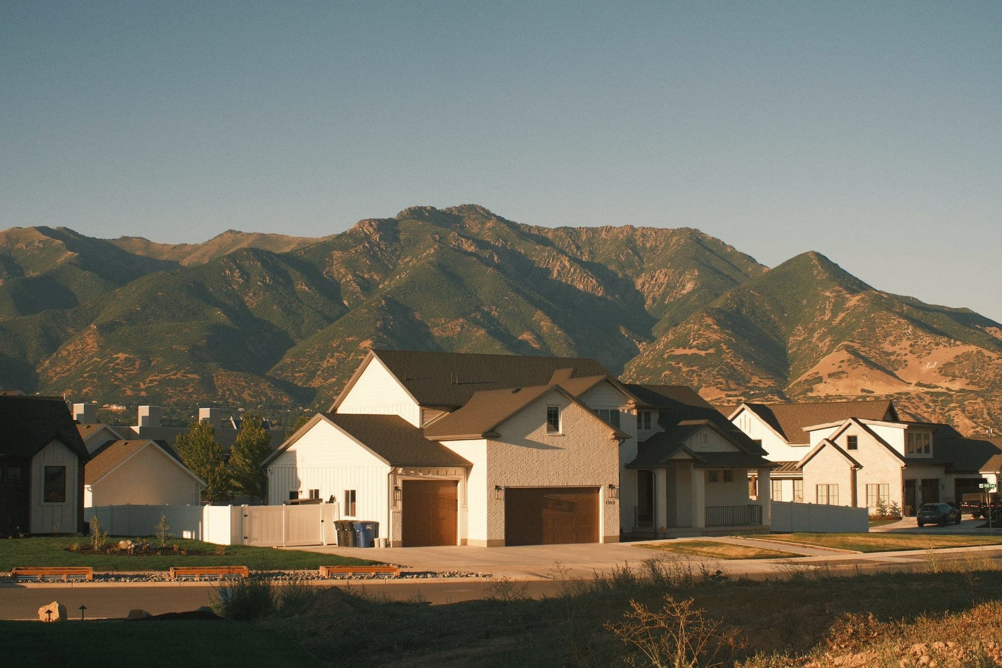 A row of new two-story homes below a mountain range in evening light